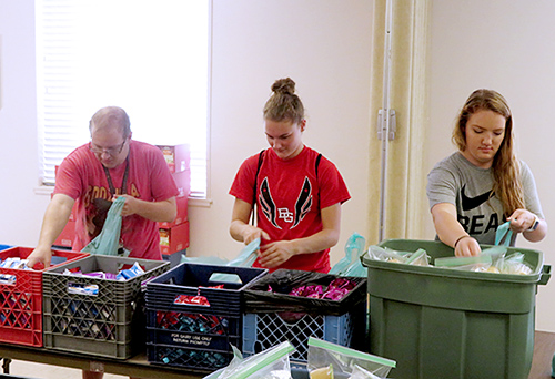 Three students filling bags with food from crates